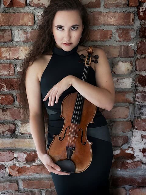 Die Geigerin Lucie Bartholomäi mit ihrer Violine vor einer Backsteinwand – zu Gast bei Elysium Concerts im Schloss Nymphenburg München